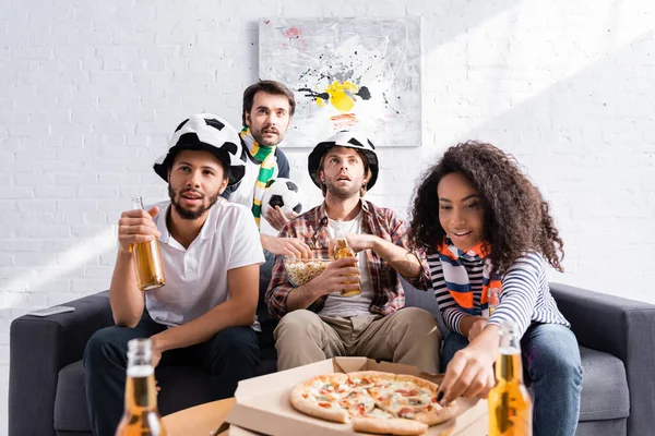 Mujer afroamericana tomando pizza cerca de amigos multiétnicos viendo campeonato de fútbol, borrosa primer plano - foto de stock