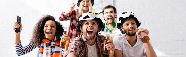 Amigos emocionados en los aficionados al fútbol sombreros gritando mientras ve la competencia de fútbol, pancarta - foto de stock