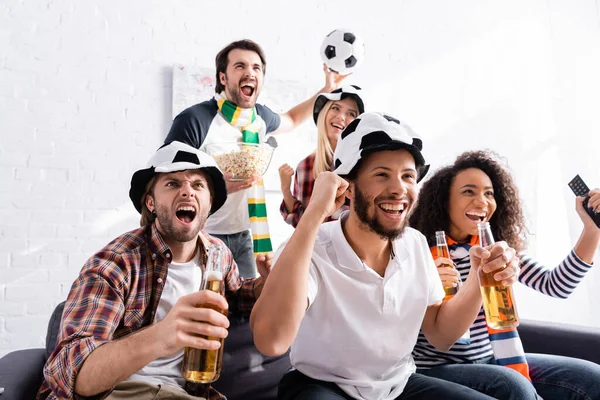 Alegres fanáticos del fútbol sosteniendo cerveza y mostrando un gesto de victoria mientras miran el campeonato - foto de stock
