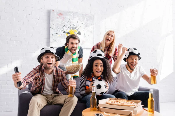 Взволнованные мультикультурные друзья смотрят чемпионат по футболу и показывают победный жест — стоковое фото