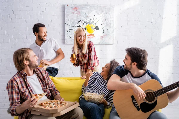 Joven tocando la guitarra acústica cerca de amigos multiétnicos felices durante la fiesta - foto de stock