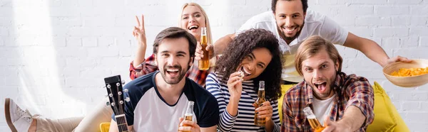 Donna sorridente che mostra il gesto della vittoria vicino ad amici eccitati che tengono la birra durante la festa, banner — Foto stock