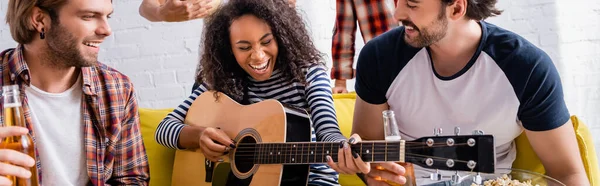 Laughing african american woman playing guitar to multicultural friends on blurred background, banner — Stock Photo