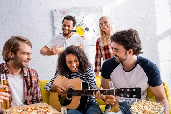 Donna afro-americana che ride mentre suona la chitarra acustica agli amici multietnici durante la festa — Foto stock