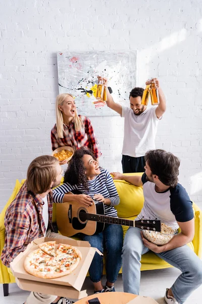 Cheerful african american man holding bottles of beer near excited multicultural friends — Stock Photo
