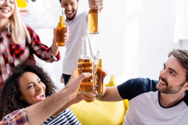 Aufgeregte multiethnische Freunde, die während einer Party Bierflaschen klappern, verschwommener Hintergrund — Stockfoto