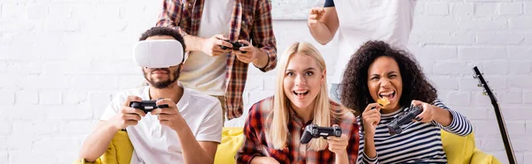 KYIV, UKRAINE - OCTOBER 19, 2020: cheerful african american woman eating chips while playing video game with multicultural friends — Stock Photo