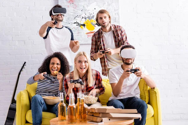 KYIV, UKRAINE - OCTOBER 19, 2020: cheerful multiethnic friends using vr headsets and playing video game during party — Stock Photo