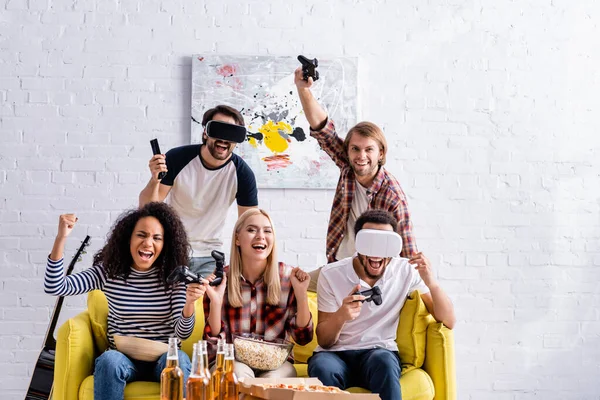 KYIV, UKRAINE - OCTOBER 19, 2020: happy multiethnic friends showing win gesture while holding joysticks during party — Stock Photo