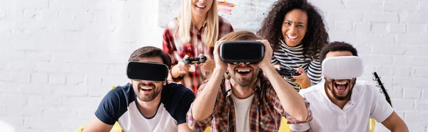 KYIV, UKRAINE - OCTOBER 19, 2020: excited multicultural men using vr headsets near women playing video game, banner — Stock Photo