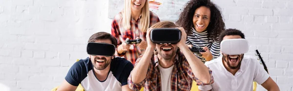 KYIV, UKRAINE - 19 OCTOBRE 2020 : hommes multiculturels excités utilisant des casques vr près des femmes jouant à un jeu vidéo, bannière — Photo de stock