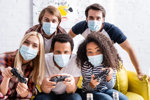 KYIV, UCRAINA - 19 OTTOBRE 2020: amici multietnici concentrati in maschere mediche che giocano ai videogiochi durante la festa — Foto stock