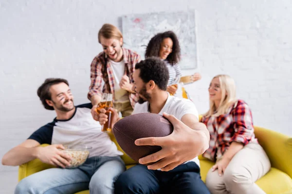 Uomo afroamericano in possesso di palla da rugby vicino amici multiculturali con facce dipinte su sfondo sfocato — Foto stock