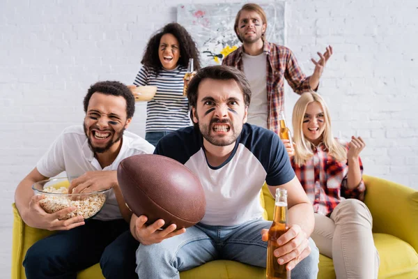Multicultural rugby fans with painted faces grimacing while watching championship at home — Stock Photo