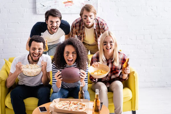 African american woman holding rugby ball and shouting while watching championship with excited multiethnic friends — Stock Photo