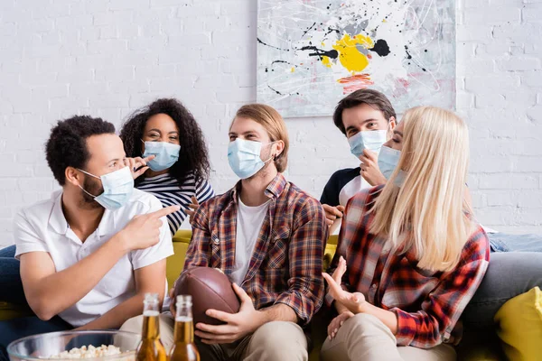 African american man pointing with finger near multicultural friends in medical masks on blurred foreground — Stock Photo