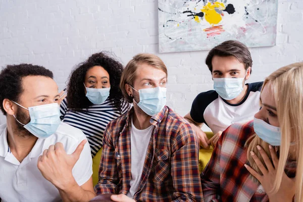 African american man pointing with thumb at woman with hand on chest near multicultural friends in medical masks — Stock Photo