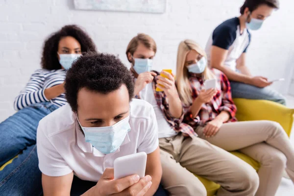 African american man in medical masks chatting on mobile phone near multicultural friends on blurred background — Stock Photo