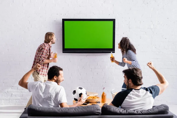 Excités amis multiculturels montrant geste de victoire tout en regardant le championnat de football à la télévision — Photo de stock