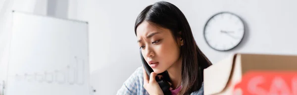 Worried asian volunteer talking on telephone with blurred carton box on foreground, banner — Stock Photo