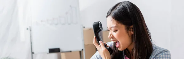 Aggressive asiatische Freiwillige schreien am Handy mit verschwommenem Charity Center im Hintergrund, Banner — Stockfoto