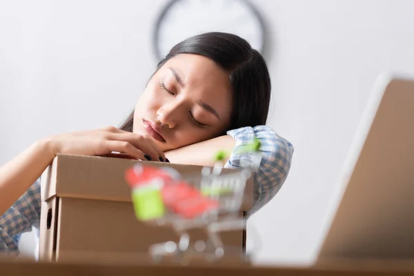 Volontaire asiatique aux yeux fermés appuyé sur une boîte en carton avec un panier flou au premier plan — Photo de stock