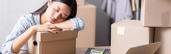 Fatigué asiatique volontaire dormir sur carton boîte tandis que assis au bureau au centre de charité sur fond flou, bannière — Photo de stock