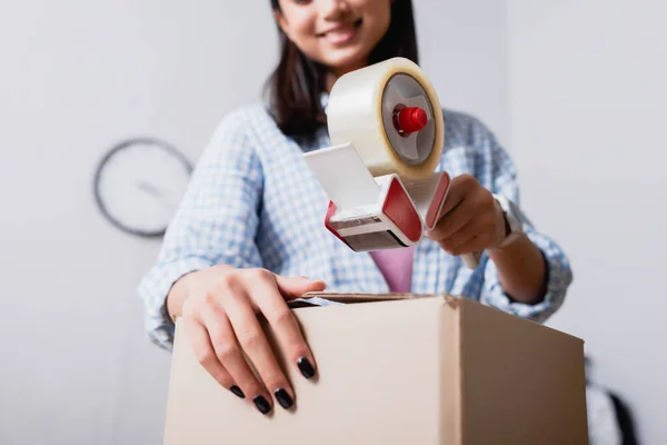 Vue recadrée du volontaire féminin avec boîte en carton de fermeture du distributeur de scotch sur fond flou — Photo de stock