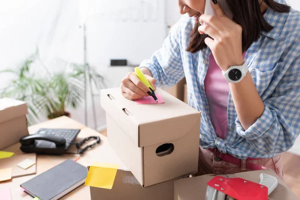 Ausgeschnittene Ansicht von Freiwilligen, die auf dem Smartphone sprechen und auf einen Zettel neben den Paketen auf dem Tisch schreiben — Stockfoto