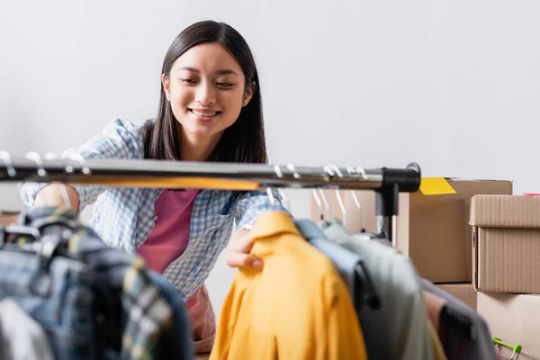 Smiling asian volunteer standing near clothes on hanging rack on blurred foreground — Stock Photo