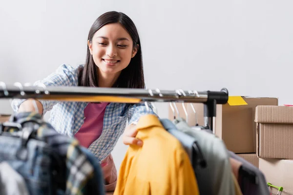 Souriant asiatique volontaire debout près de vêtements sur accrocher rack sur flou premier plan — Stock Photo