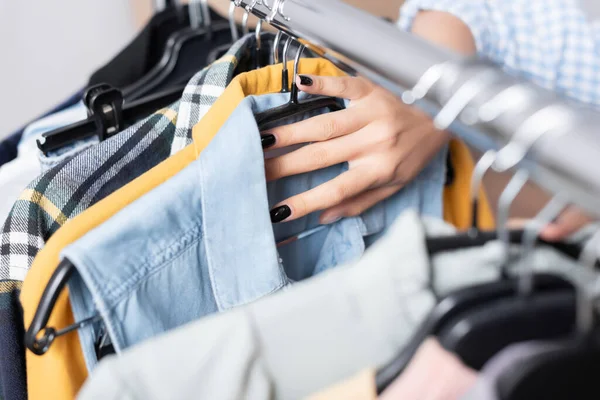 Cropped view of volunteer holding clothes on hanging rack on blurred foreground in charity center — Stock Photo
