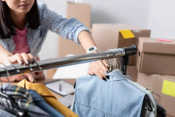 Cropped view of volunteer standing near clothes on hangers on hanging rack in charity office — Stock Photo