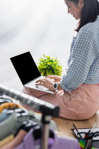 Lächelnder asiatischer Manager mit Laptop und leerem Bildschirm in der Nähe von Hängegestell auf verschwommenem Vordergrund in Charity Center — Stockfoto