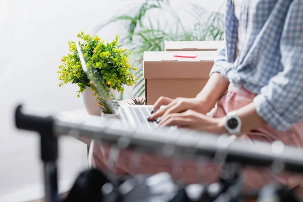 Cropped view of boxes and plants near volunteer using laptop and hanging rack on blurred foreground — Stock Photo