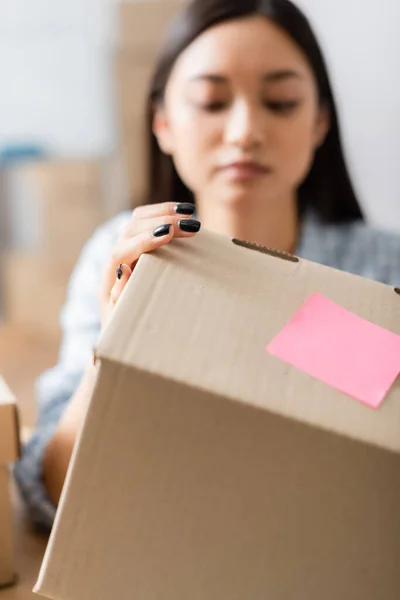 Caja de cartón con nota adhesiva en la mano de un voluntario asiático sobre fondo borroso - foto de stock