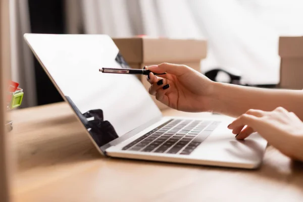 Cropped view of volunteer pointing with pen at laptop with blank screen near boxes on blurred background — Stock Photo