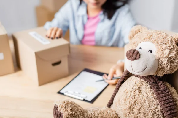 Peluche près de bénévole avec boîtes et presse-papiers sur fond flou — Photo de stock