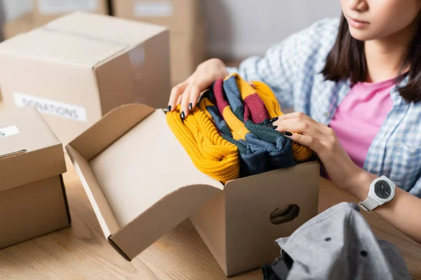 Vista recortada de voluntarios poniendo ropa en el paquete cerca de cajas en el centro de caridad - foto de stock