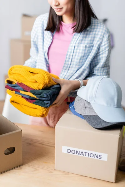 Ausgeschnittene Ansicht von Freiwilligen, die Kleidung in der Nähe von Mützen und Schachteln mit Spendenaufdruck halten — Stockfoto