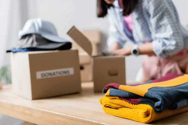 Vêtements sur la table près de bénévoles et des boîtes sur fond flou dans le centre de bienfaisance — Photo de stock