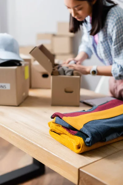 Kleidung auf Tisch in der Nähe einer Verpackungsbox im Freiwilligenzentrum auf verschwommenem Hintergrund — Stockfoto