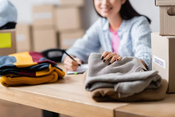 Vue recadrée de la femme tenant des vêtements près des emballages en carton sur fond flou sur la table — Photo de stock