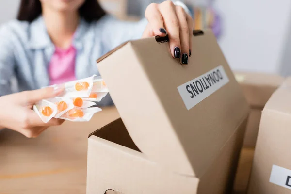 Ausgeschnittene Ansicht einer Frau, die Spritzen in eine Schachtel mit Spendenaufdruck auf verschwommenem Hintergrund legt — Stockfoto