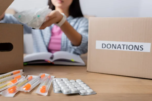 Pillole e siringhe sul tavolo vicino al volontario e scatole con lettere di donazioni su sfondo sfocato — Foto stock