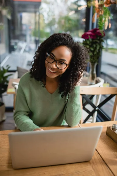 Glückliche Afroamerikanerin mit Brille blickt in Café auf Laptop — Stockfoto