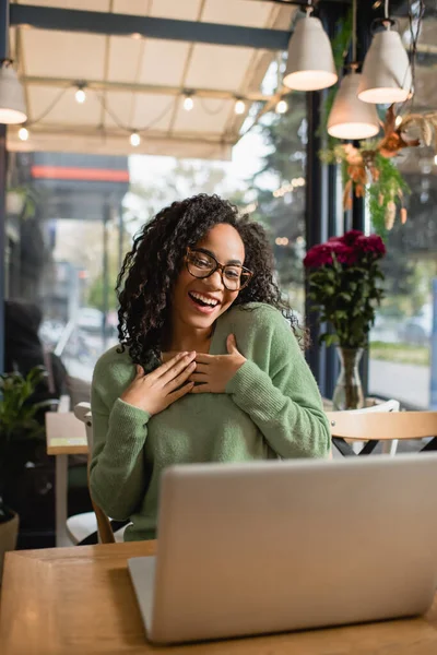 Geschmeichelte Afroamerikanerin mit Brille blickt auf Laptop auf verschwommenem Vordergrund — Stockfoto