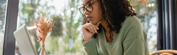 Концентрированная африканская американка в очках, смотрит на ноутбук, баннер — стоковое фото