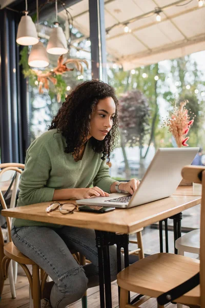 Mulher afro-americana focada usando laptop no café — Fotografia de Stock