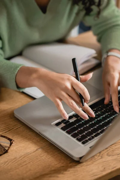 Partial view of african american woman holding pen while typing on laptop keyboard — Stock Photo